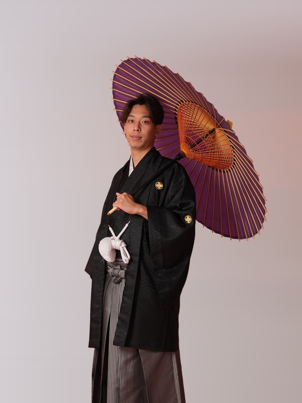 紫の和傘を持つ紋付袴姿の新郎